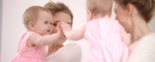 Moeder en haar baby van 15 weken oud hebben samen interactie voor een spiegel.