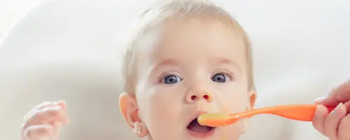 Baby van 16 weken oud maakt kennis met vast eten en neemt een proefhapje van een lepel