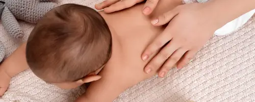Baby ligt met zijn buik op een zacht matje en speelt vliegtuigje met zijn moeder.