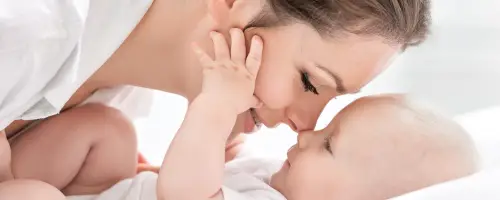Baby van 8 weken oud ligt samen met haar moeder op bed terwijl ze contact maken