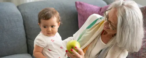 Baby van 15 weken oud zit een beetje verlegen op de schoot van haar oma.