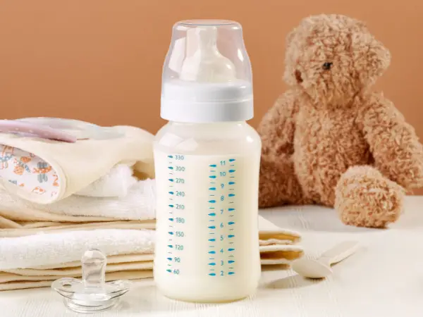 Brede babyfles met melk naast speen en knuffelbeer